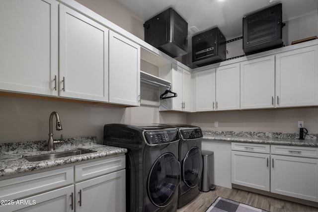 clothes washing area with cabinet space, independent washer and dryer, light wood-style flooring, and a sink