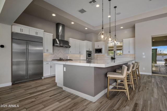 kitchen with visible vents, built in appliances, wall chimney exhaust hood, and white cabinetry