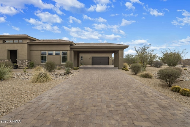 prairie-style home featuring decorative driveway, stone siding, an attached garage, and stucco siding