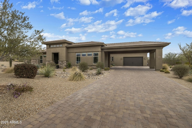 prairie-style home with stone siding, stucco siding, decorative driveway, and a garage