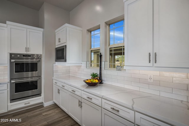 kitchen with stainless steel double oven, built in microwave, tasteful backsplash, and white cabinetry