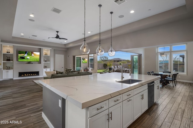 kitchen featuring wood finish floors, a sink, open floor plan, a lit fireplace, and white cabinets