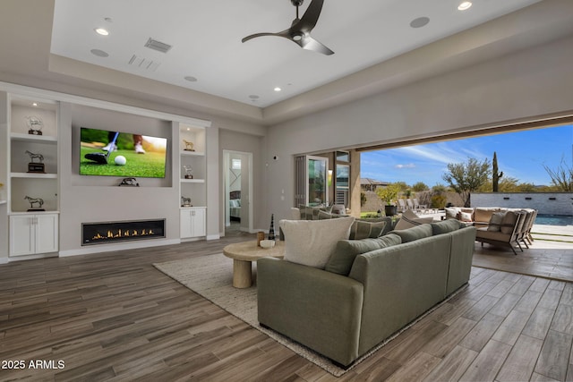 living area featuring a glass covered fireplace, built in features, wood finished floors, and visible vents