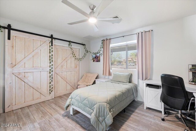 bedroom featuring ceiling fan, light wood-type flooring, and a barn door