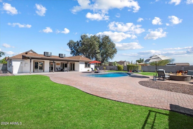 rear view of property with central AC unit, a fenced in pool, a patio area, a lawn, and an outdoor fire pit