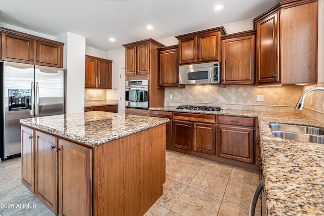 kitchen with stainless steel appliances, a sink, a center island, light stone counters, and backsplash