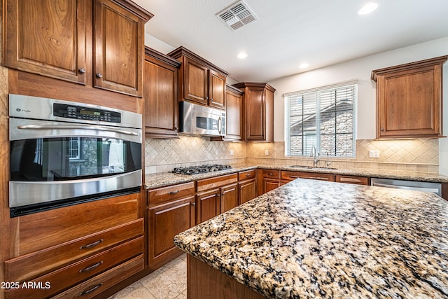 kitchen featuring stainless steel appliances, light stone countertops, a sink, recessed lighting, and decorative backsplash