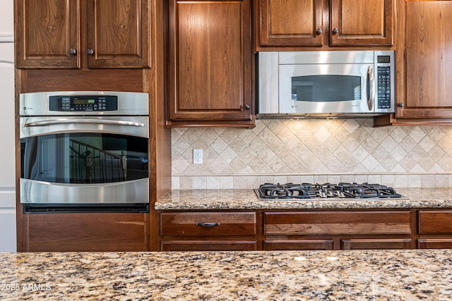 kitchen with stainless steel appliances, light stone counters, and decorative backsplash