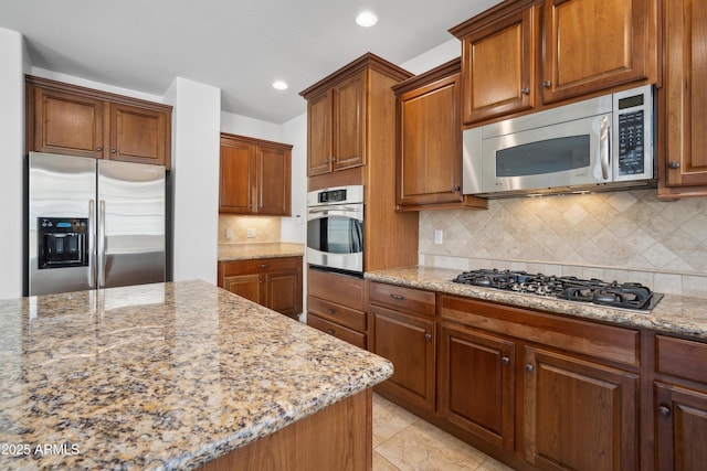 kitchen featuring appliances with stainless steel finishes, light stone countertops, recessed lighting, backsplash, and brown cabinets