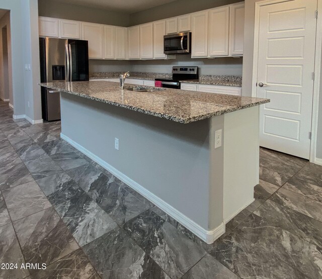 kitchen featuring stainless steel appliances, dark stone counters, white cabinetry, sink, and a kitchen island with sink