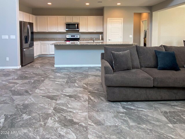 kitchen featuring stainless steel appliances, a center island with sink, light stone counters, white cabinets, and sink