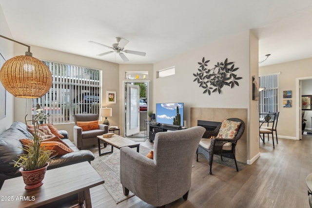 living room with a tiled fireplace, ceiling fan, and wood-type flooring