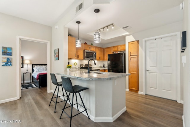 kitchen featuring kitchen peninsula, a kitchen breakfast bar, stainless steel appliances, decorative light fixtures, and hardwood / wood-style flooring