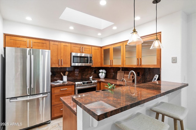 kitchen featuring decorative light fixtures, dark stone countertops, a kitchen bar, kitchen peninsula, and stainless steel appliances