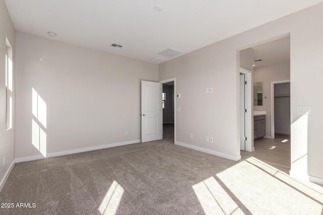 unfurnished bedroom with light colored carpet, visible vents, baseboards, and ensuite bathroom