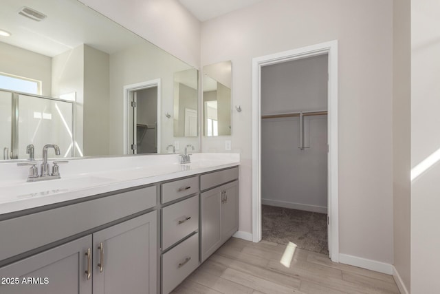 bathroom with a walk in closet, double vanity, visible vents, a stall shower, and a sink