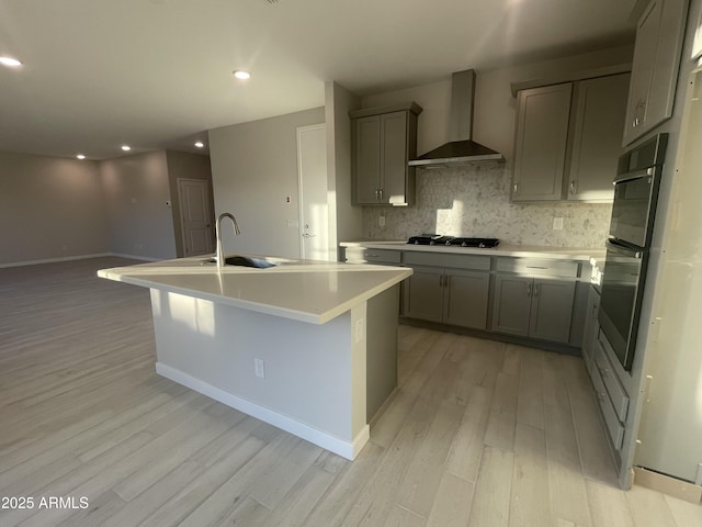 kitchen with light wood-style flooring, a sink, wall chimney range hood, appliances with stainless steel finishes, and tasteful backsplash