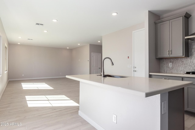 kitchen featuring light wood-type flooring, gray cabinets, a sink, and an island with sink