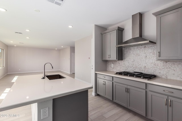 kitchen with visible vents, wall chimney exhaust hood, gray cabinets, stainless steel gas stovetop, and a sink