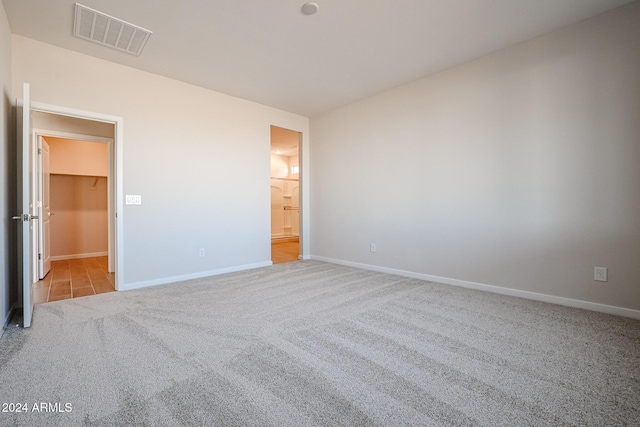 unfurnished bedroom featuring a walk in closet, light colored carpet, and a closet