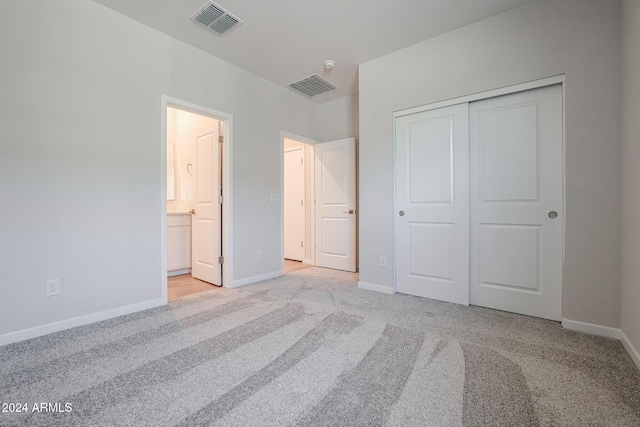 unfurnished bedroom with light colored carpet, a closet, and ensuite bathroom