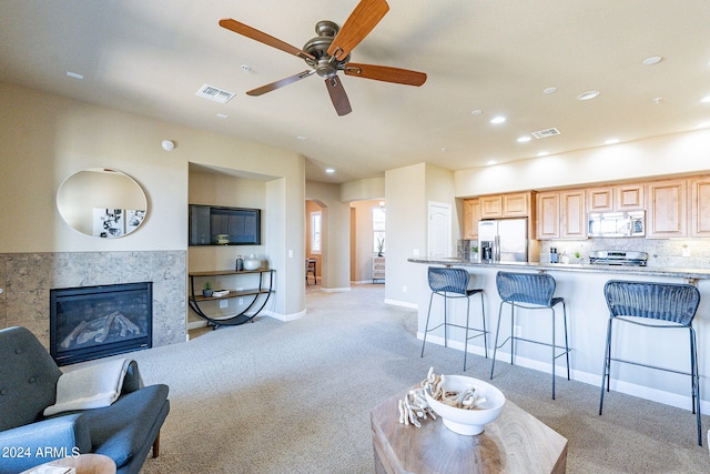 carpeted living room with a tile fireplace and ceiling fan