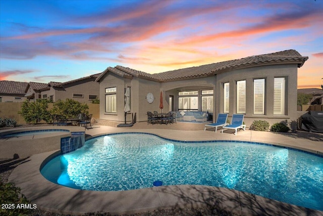 back house at dusk with a swimming pool with hot tub and a patio