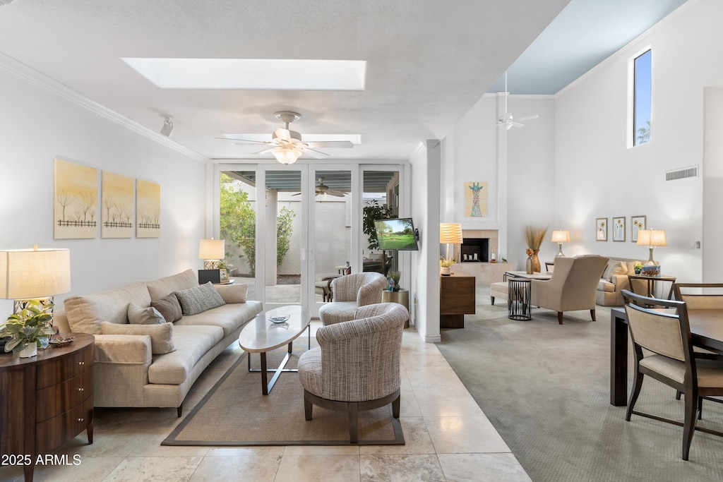 living area featuring visible vents, crown molding, ceiling fan, a fireplace, and a skylight