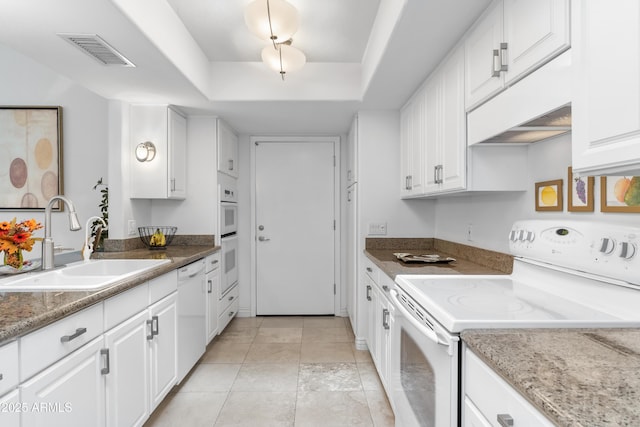 kitchen featuring white appliances, visible vents, a tray ceiling, a sink, and white cabinets