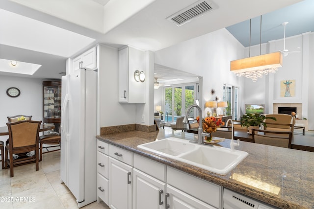 kitchen with visible vents, a sink, white cabinetry, freestanding refrigerator, and a fireplace