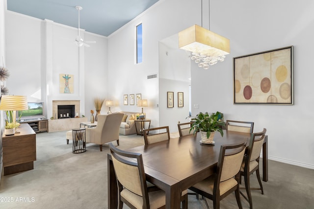 carpeted dining area with visible vents, ceiling fan with notable chandelier, a high end fireplace, crown molding, and a towering ceiling