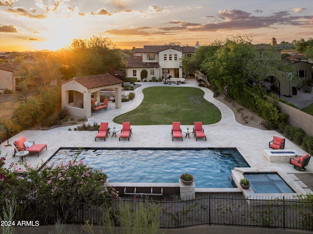 pool at dusk with an in ground hot tub, a patio area, a gazebo, an outdoor living space with a fire pit, and a lawn