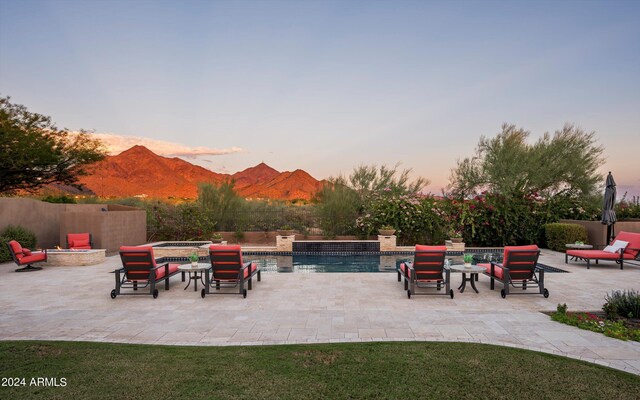 pool at dusk featuring an in ground hot tub and a patio