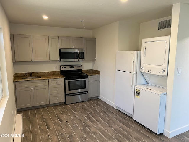 kitchen with sink, dark wood-type flooring, stacked washing maching and dryer, appliances with stainless steel finishes, and gray cabinetry