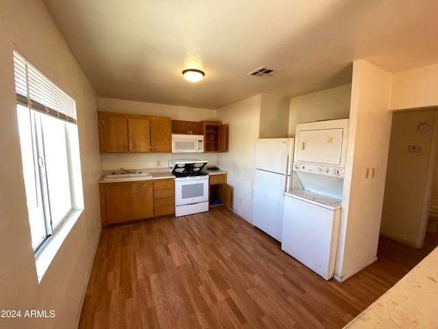 kitchen featuring white appliances, wood-type flooring, sink, and stacked washer and dryer