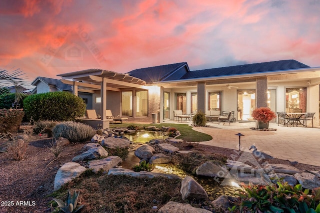 back of property at dusk featuring a patio, stucco siding, and a pergola