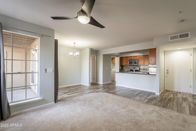 unfurnished living room with dark colored carpet and ceiling fan with notable chandelier