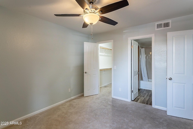 unfurnished bedroom featuring carpet, a walk in closet, ensuite bath, ceiling fan, and a closet