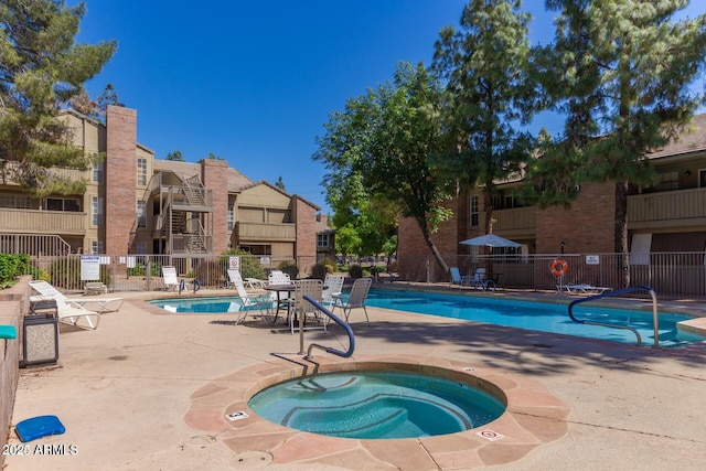 pool with a patio area, a community hot tub, and fence