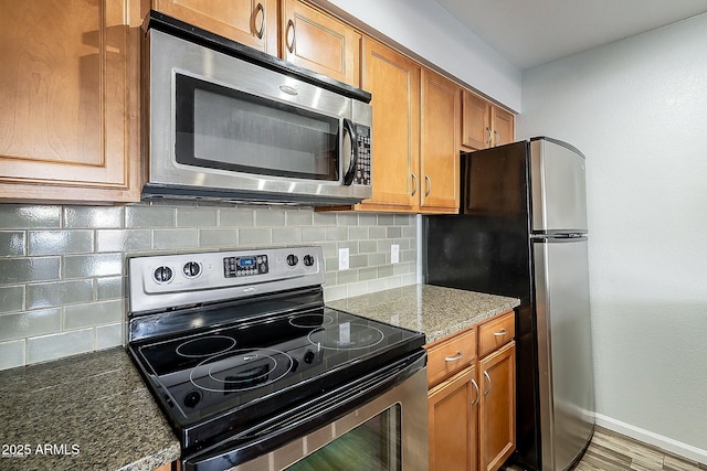 kitchen with wood-type flooring, backsplash, stainless steel appliances, and dark stone countertops