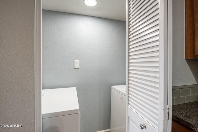 clothes washing area featuring a textured wall, laundry area, and washing machine and clothes dryer