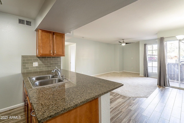 kitchen featuring a ceiling fan, brown cabinetry, visible vents, a sink, and tasteful backsplash