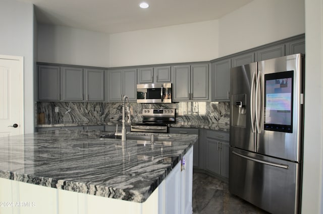 kitchen with dark stone countertops, backsplash, appliances with stainless steel finishes, and gray cabinetry