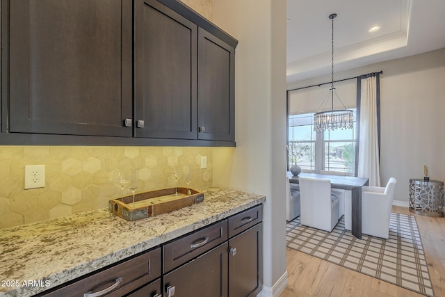 8768 E Granite Pass Rd, Scottsdale, AZ 85266 - kitchen featuring light wood-style flooring, a chandelier, light stone countertops, dark brown cabinets, and a raised ceiling