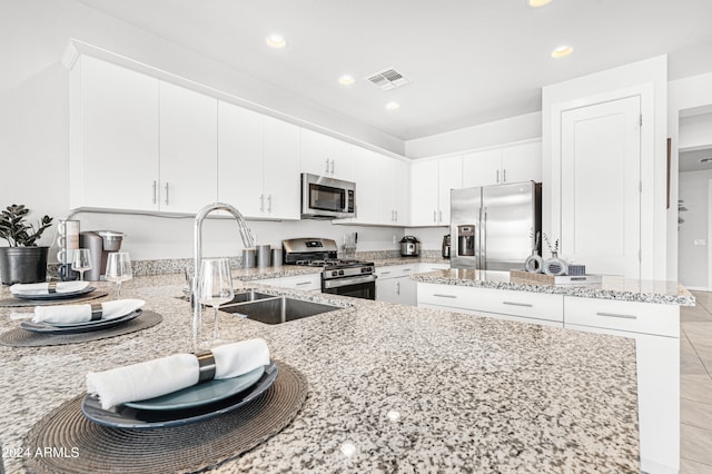 kitchen with appliances with stainless steel finishes, white cabinetry, sink, and light stone countertops