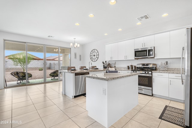 kitchen with pendant lighting, white cabinetry, a kitchen island, light stone countertops, and appliances with stainless steel finishes