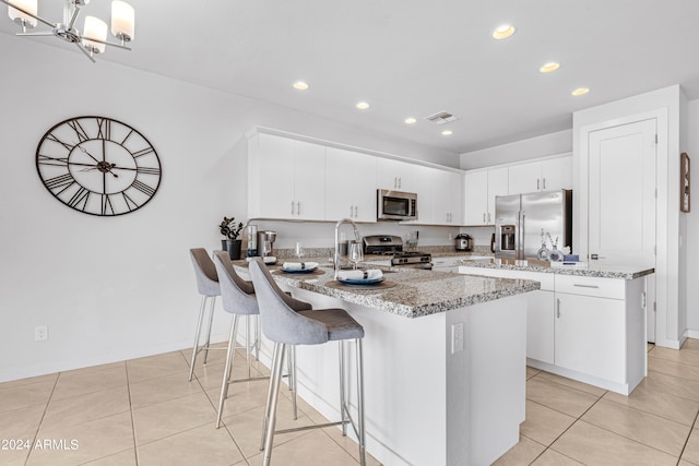 kitchen featuring an island with sink, light stone counters, appliances with stainless steel finishes, and white cabinetry