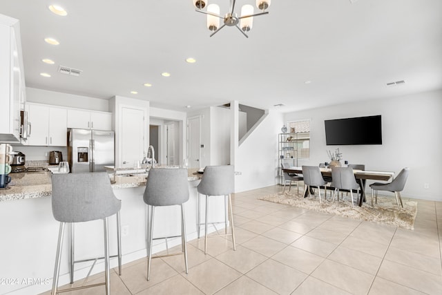 kitchen featuring stainless steel fridge, light stone countertops, a notable chandelier, kitchen peninsula, and white cabinets