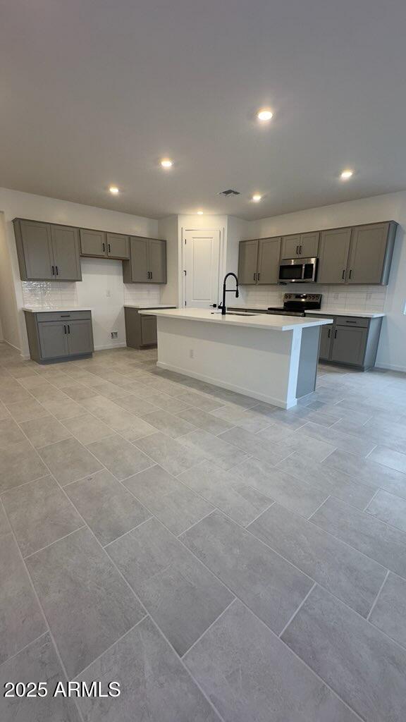 kitchen with sink, gray cabinetry, a kitchen island with sink, and stainless steel appliances