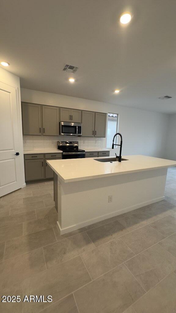 kitchen featuring appliances with stainless steel finishes, an island with sink, sink, gray cabinets, and light tile patterned flooring